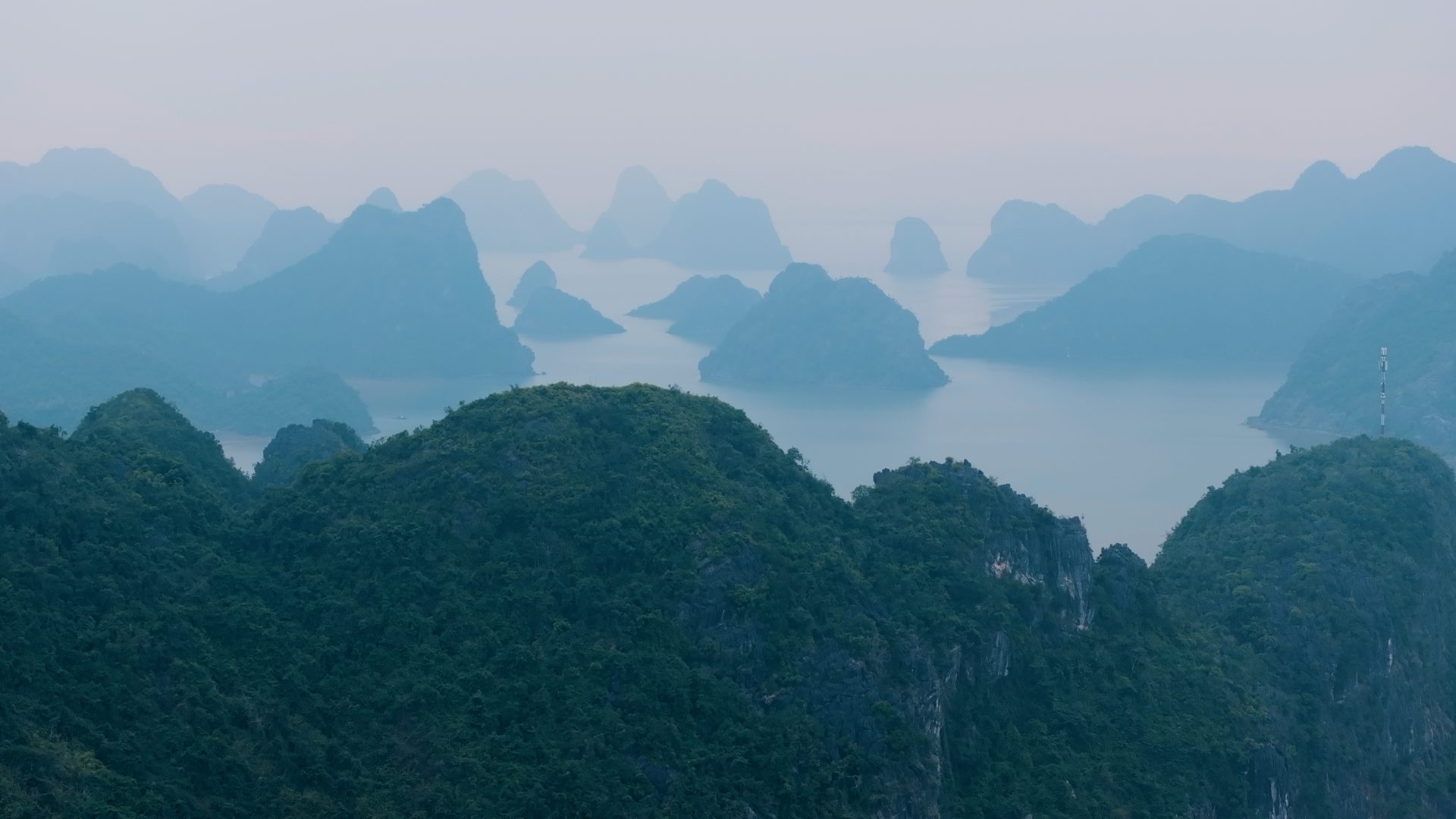 Ha Long Bay in haze: forested limestone towers receding across still water.